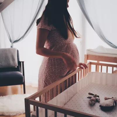 pregnant woman looks down at an empty crib
