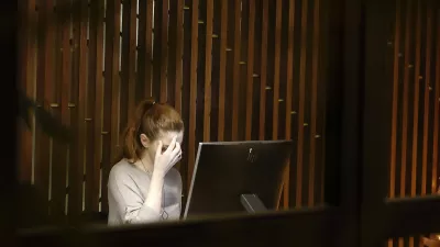 A woman sitting in front of a computer screen with her hand at her forehead